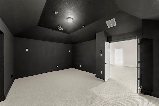 carpeted home theater room with lofted ceiling, baseboards, and visible vents