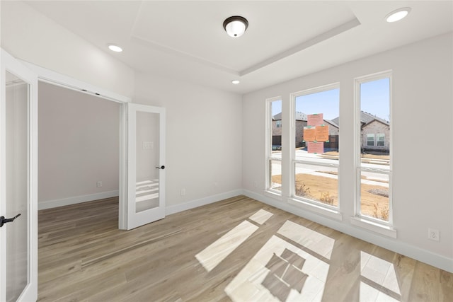 unfurnished room with a tray ceiling, light wood-style flooring, and baseboards