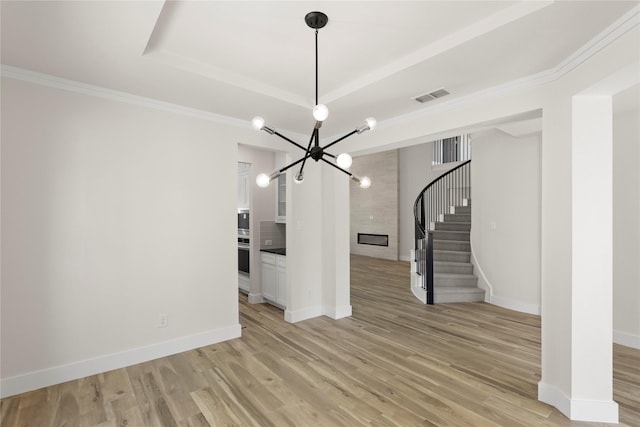 unfurnished living room with visible vents, a chandelier, stairway, light wood-style flooring, and a raised ceiling