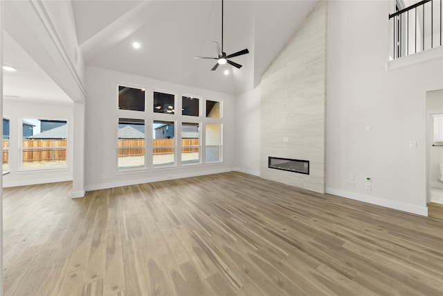 unfurnished living room featuring light wood-style flooring, baseboards, high vaulted ceiling, and ceiling fan