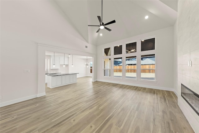 unfurnished living room with high vaulted ceiling, baseboards, light wood-style floors, and a ceiling fan