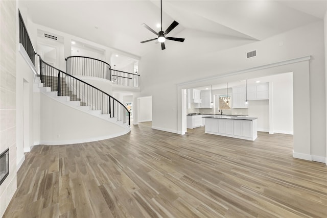 unfurnished living room with stairs, light wood-style flooring, visible vents, and a sink