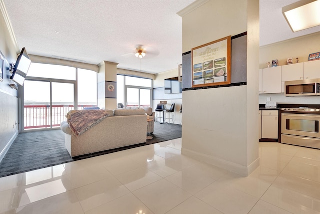 living area featuring baseboards, ceiling fan, ornamental molding, light tile patterned flooring, and a textured ceiling