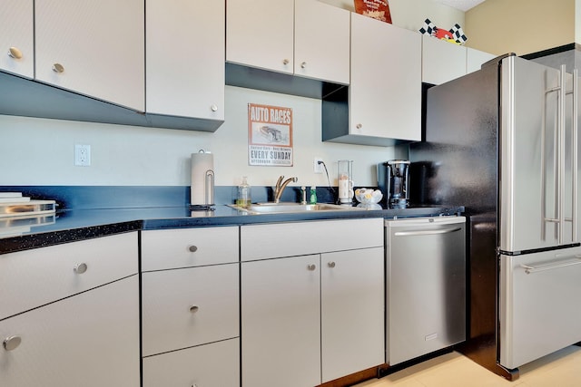 kitchen featuring dark countertops, white cabinets, stainless steel appliances, and a sink