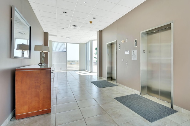 hall with elevator, light tile patterned floors, and a drop ceiling