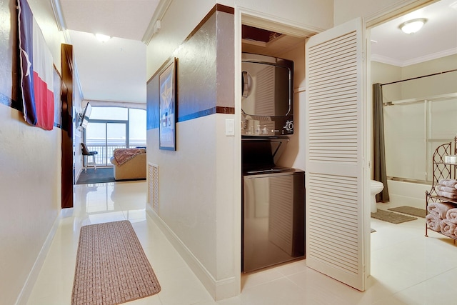 hallway with tile patterned flooring, stacked washer and dryer, baseboards, and ornamental molding