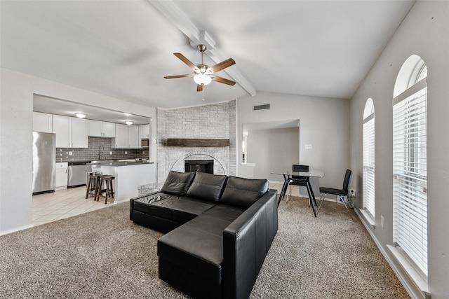 living area with a ceiling fan, visible vents, vaulted ceiling with beams, a fireplace, and light colored carpet