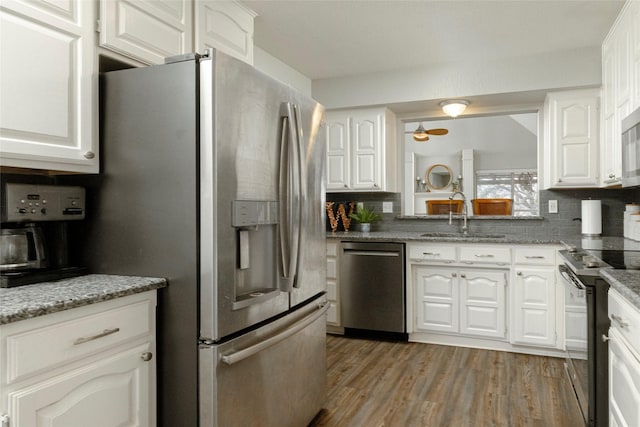 kitchen featuring a sink, wood finished floors, stainless steel appliances, white cabinets, and decorative backsplash