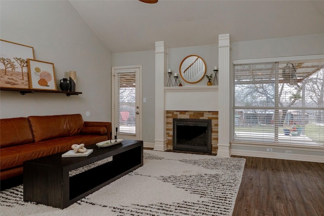 living area with vaulted ceiling, a stone fireplace, baseboards, and wood finished floors