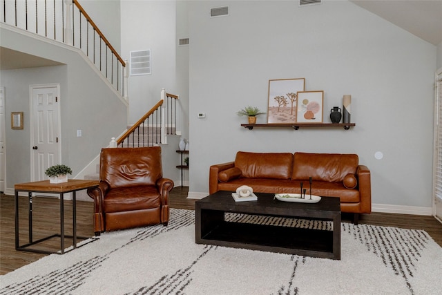 living area with visible vents, wood finished floors, baseboards, a towering ceiling, and stairs