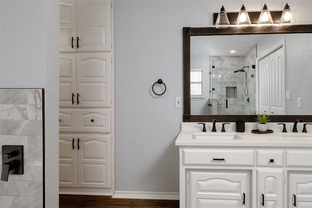 bathroom with baseboards, double vanity, a stall shower, wood finished floors, and a sink