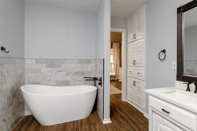 bathroom featuring a wainscoted wall, wood finished floors, tile walls, a freestanding bath, and vanity