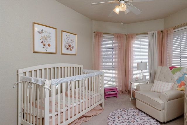 carpeted bedroom with ceiling fan and a nursery area