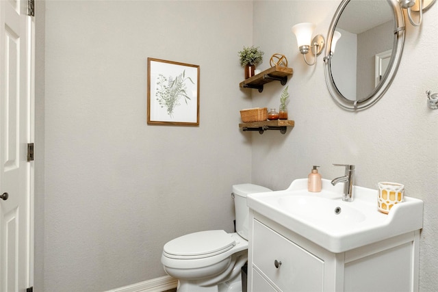 half bath with baseboards, toilet, and vanity