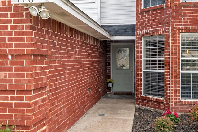 view of exterior entry featuring brick siding and a shingled roof