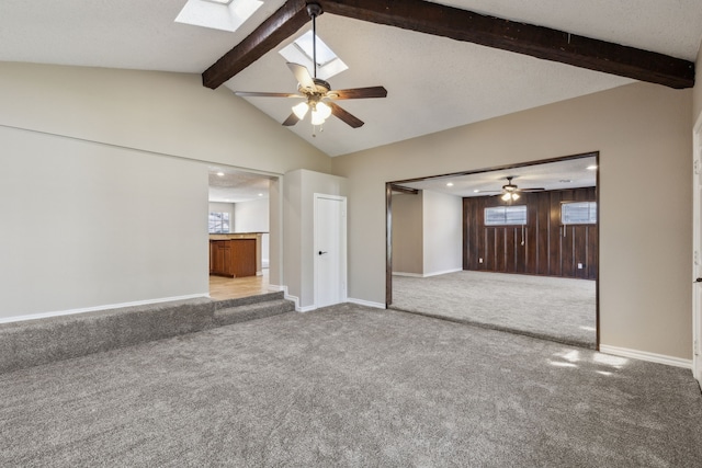 unfurnished living room featuring vaulted ceiling with skylight, baseboards, carpet, and ceiling fan