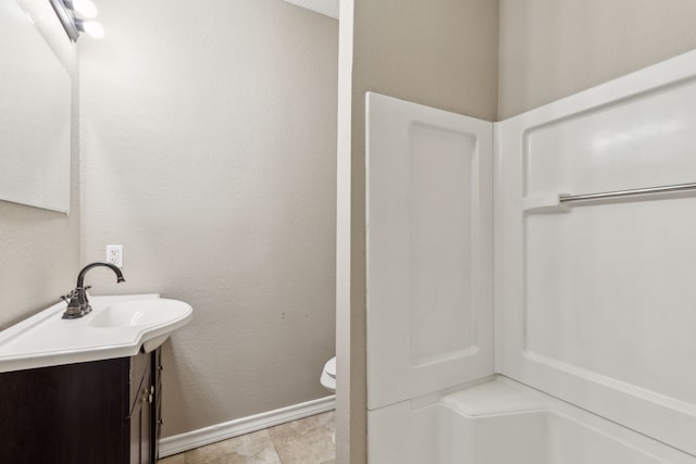 full bathroom with baseboards, toilet, vanity, and a textured wall