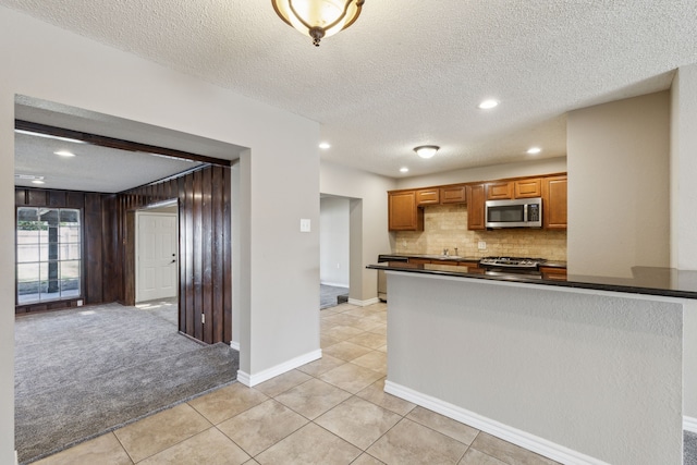 kitchen with light carpet, a sink, stainless steel microwave, dark countertops, and decorative backsplash