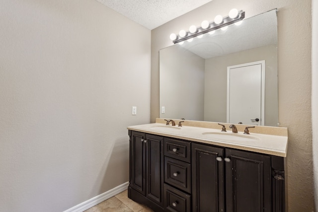 bathroom with a sink, a textured ceiling, double vanity, and tile patterned floors