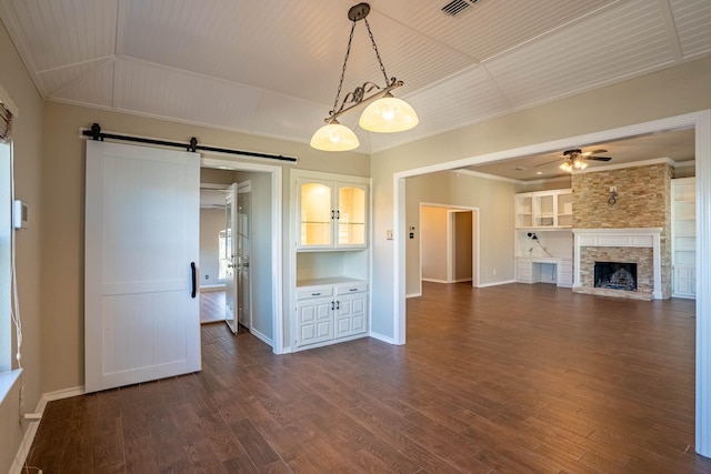 unfurnished living room featuring ornamental molding, a ceiling fan, dark wood finished floors, a barn door, and baseboards