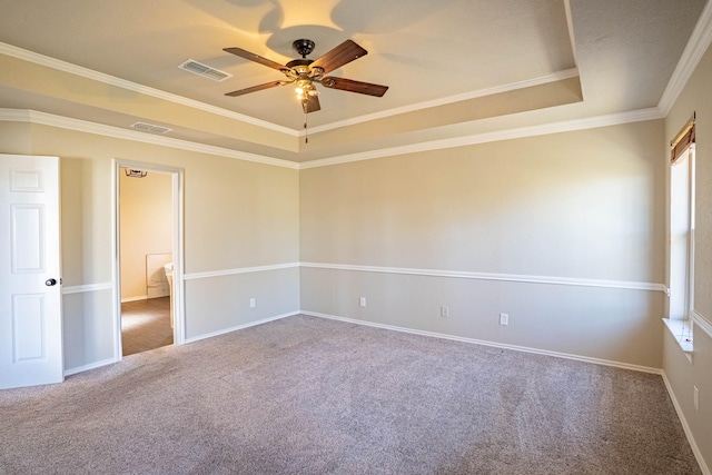 carpeted empty room featuring visible vents, ceiling fan, baseboards, a tray ceiling, and ornamental molding