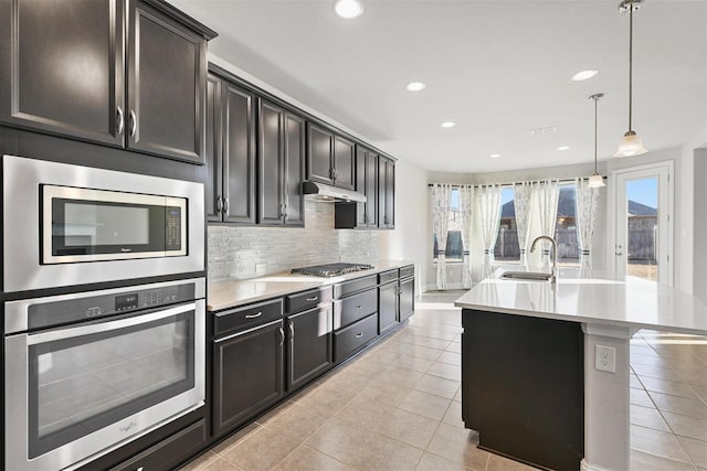 kitchen with a sink, light countertops, under cabinet range hood, appliances with stainless steel finishes, and tasteful backsplash