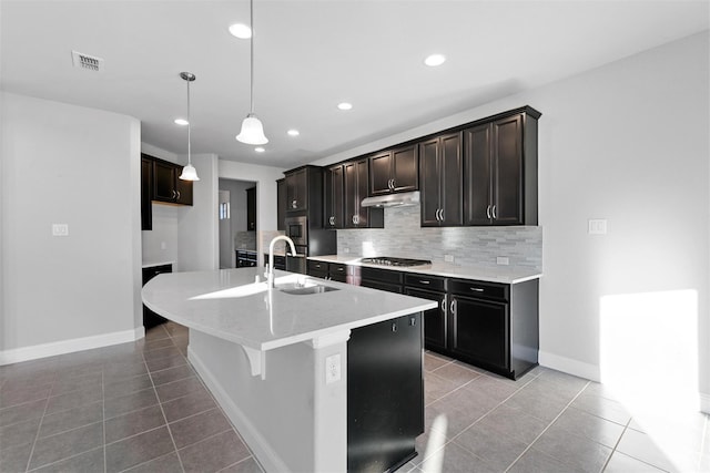 kitchen with a sink, decorative backsplash, appliances with stainless steel finishes, light tile patterned flooring, and a kitchen island with sink