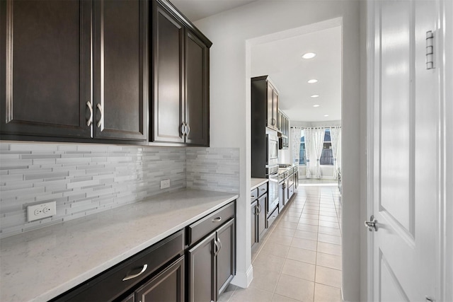 kitchen featuring light stone countertops, light tile patterned flooring, recessed lighting, dark brown cabinetry, and backsplash