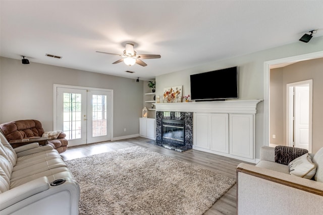 living area featuring a high end fireplace, visible vents, ceiling fan, light wood-type flooring, and french doors