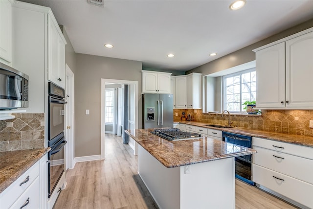 kitchen with dark stone countertops, white cabinetry, black appliances, and a sink