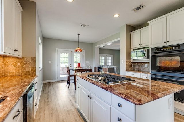 kitchen featuring visible vents, stone counters, a kitchen island, stainless steel appliances, and light wood-style floors