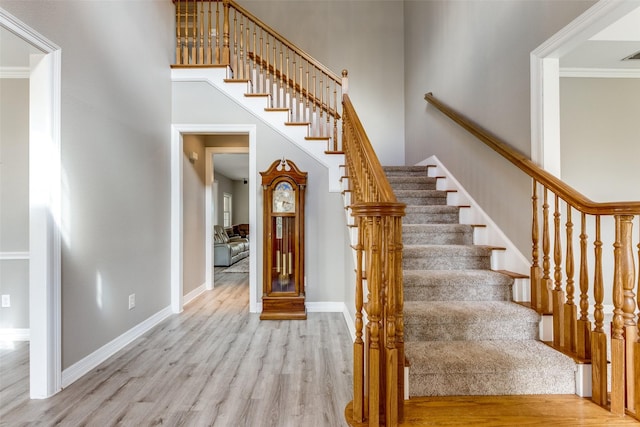 staircase featuring baseboards, a high ceiling, wood finished floors, and ornamental molding