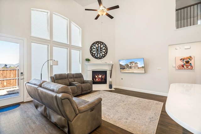 living area with a high ceiling, a fireplace with flush hearth, dark wood-style floors, and ceiling fan