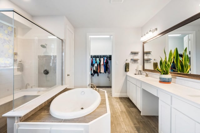 bathroom featuring a shower stall, a garden tub, double vanity, and wood finished floors