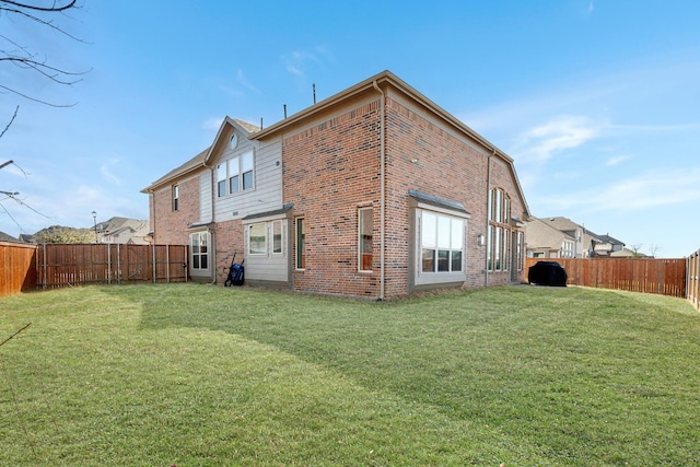 rear view of house with brick siding, a fenced backyard, and a yard