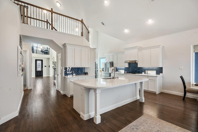 kitchen with a kitchen island with sink, white cabinets, stainless steel fridge with ice dispenser, light countertops, and dark wood-style flooring