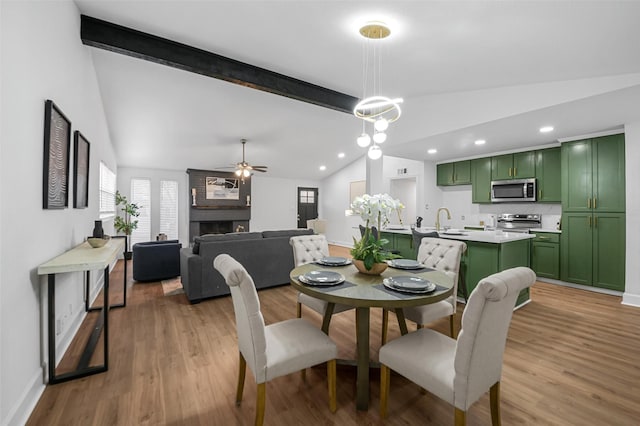 dining space featuring light wood-type flooring, a ceiling fan, a fireplace, and vaulted ceiling with beams