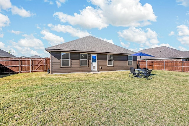 rear view of property featuring a lawn, a fenced backyard, and a shingled roof