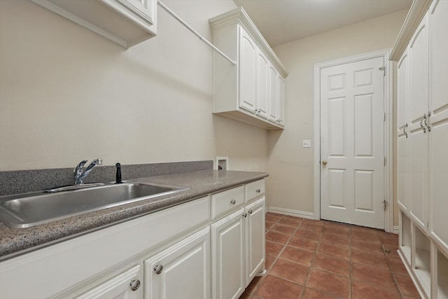 washroom featuring dark tile patterned floors, a sink, cabinet space, baseboards, and hookup for a washing machine