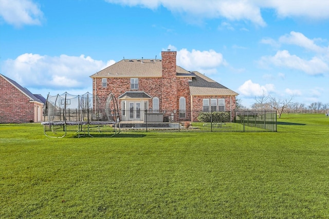 back of property with a yard, brick siding, a trampoline, and fence