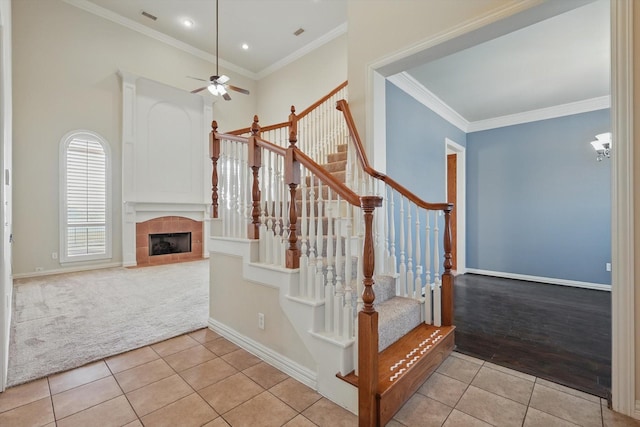 stairway with tile patterned floors, crown molding, a fireplace, and ceiling fan