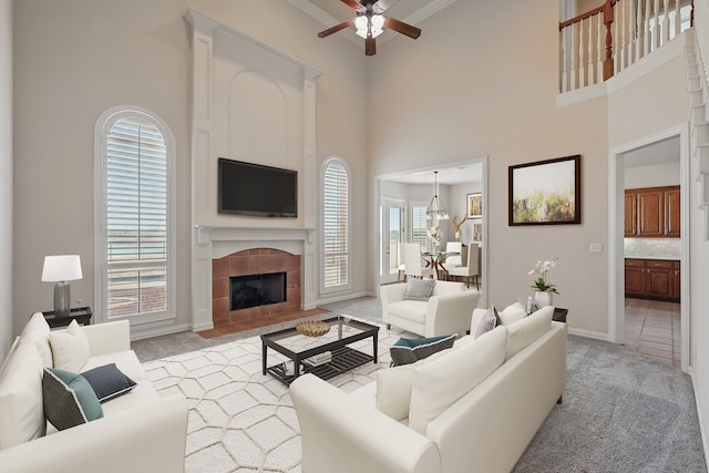 living room with a ceiling fan, light colored carpet, a towering ceiling, and a tile fireplace