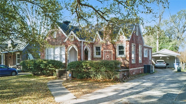 tudor-style house featuring an attached carport, brick siding, central AC, and driveway