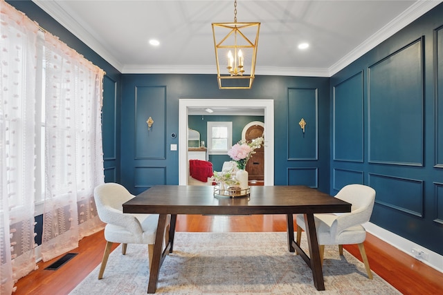 dining space with visible vents, a decorative wall, crown molding, wood finished floors, and a notable chandelier