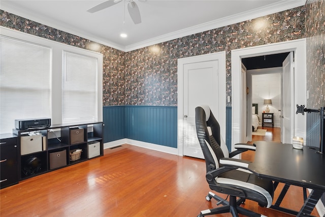 office featuring wood finished floors, a ceiling fan, a wainscoted wall, wallpapered walls, and ornamental molding