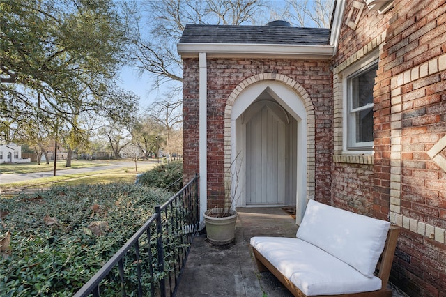 view of exterior entry featuring brick siding and a shingled roof