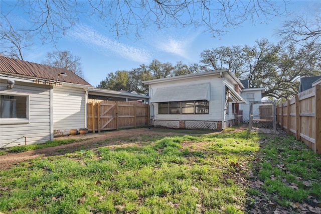 rear view of house featuring a lawn, a fenced backyard, and a gate