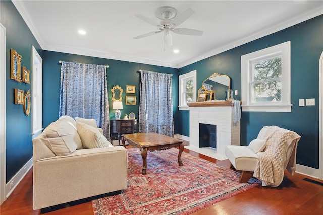 living area featuring a brick fireplace, a ceiling fan, baseboards, and ornamental molding