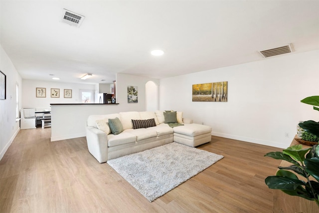 living area with wood finished floors, arched walkways, visible vents, and baseboards