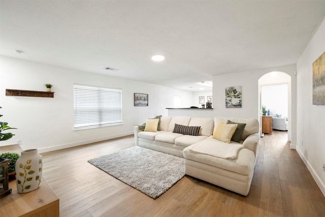 living room featuring arched walkways, visible vents, baseboards, and wood finished floors